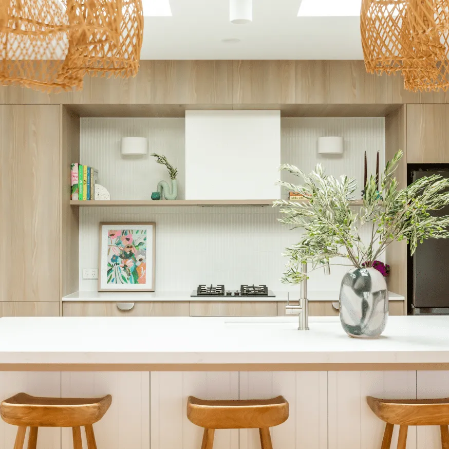 Kitchen with timber cabinetry, rattan pendant lights, white island bench and styled open shelving