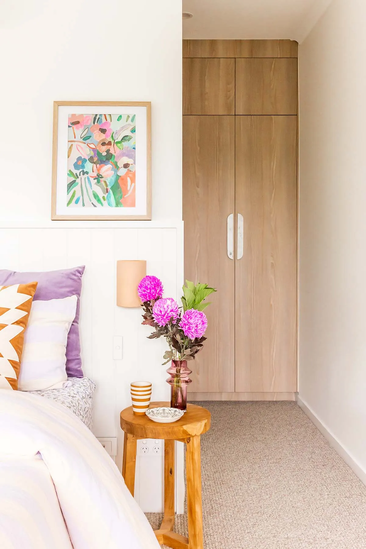Master bedroom styled with lilac cushions, a floral artwork and pink flowers