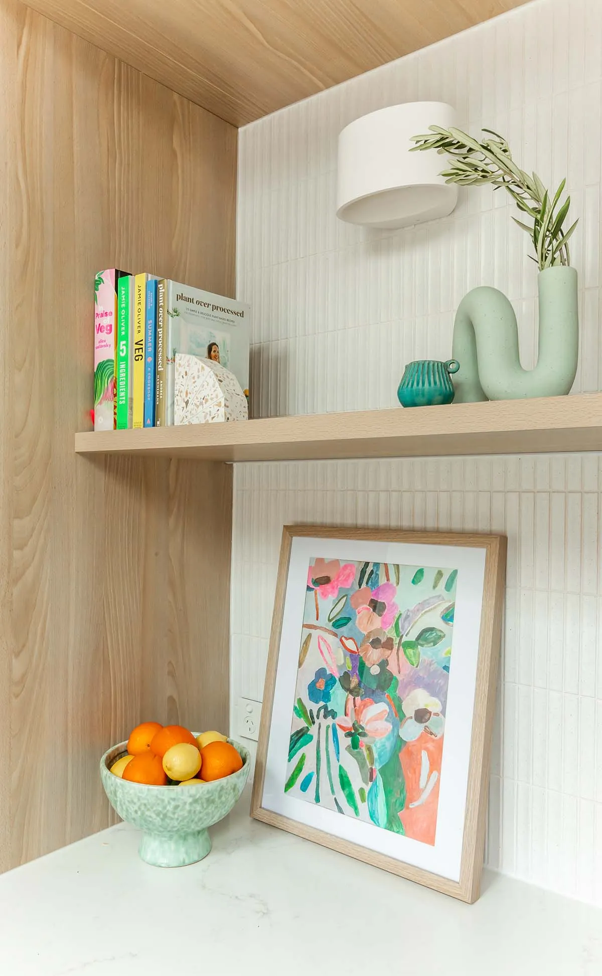 Styled timber kitchen shelf with books, a green sculptural vase and a floral artwork